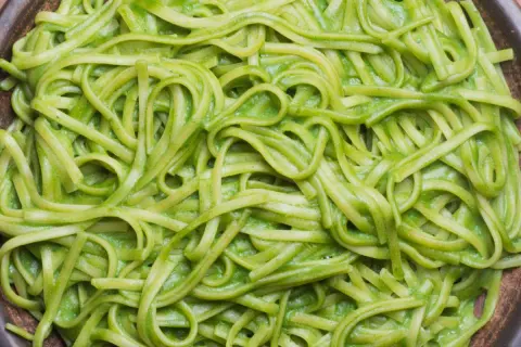 Pasta fresca condita con una cremosa salsa verde, probabilmente crema di zucchine per pasta, servita in un piatto scuro.