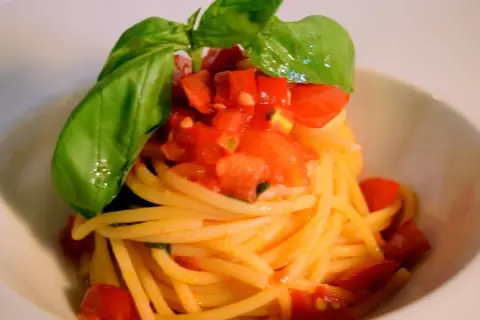 Spaghetti conditi con un fresco sugo con pomodorini freschi e basilico, un piatto semplice e gustoso.