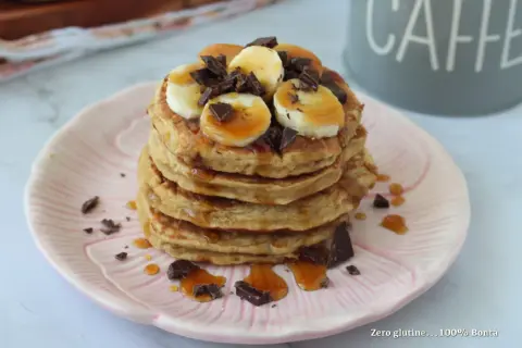 Pancake light con banana, cioccolato e sciroppo d'acero su un piatto rosa.