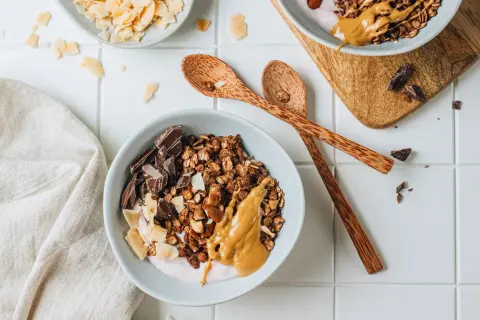 Una ciotola di granola fatta in casa con yogurt, burro di arachidi, scaglie di cocco e pezzi di cioccolato fondente.