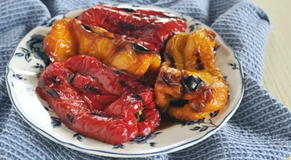 Piatto di peperoni arrostiti al forno, rossi e gialli, cotti alla perfezione, con un leggero velo di bruciatura che ne esalta il sapore.