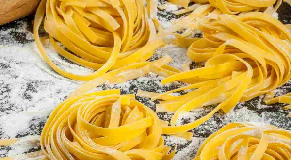 Nidi di tagliatelle fatte in casa, fresche e dorate, sparse su un piano cosparso di farina. Un invito alla tradizione culinaria.