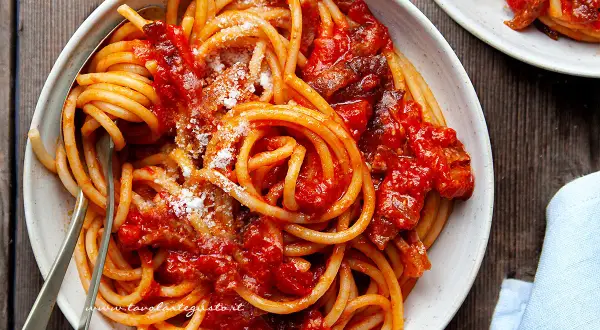 Un piatto invitante di bucatini all'amatriciana ricetta, conditi con sugo rosso e guanciale croccante, spolverati di pecorino.