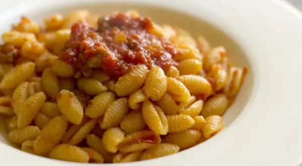 Un piatto di malloreddus alla campidanese, pasta sarda con sugo di pomodoro e salsiccia, serviti in una ciotola bianca.