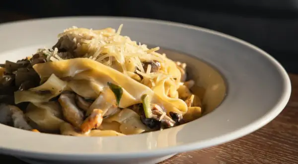 Un piatto di pasta fresca con salsiccia e funghi, condita con parmigiano grattugiato.