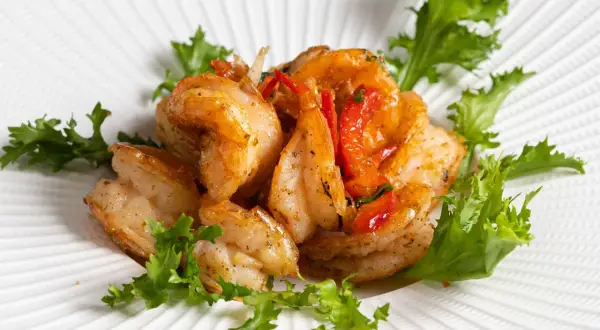 Gamberi sale e pepe succulenti, saltati con pomodorini e guarniti con insalata fresca su un piatto bianco texturizzato.