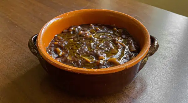 Una ciotola di terracotta piena di pasta e lenticchie, condita con olio d'oliva. Un piatto confortante e saporito.