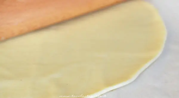Mattarello stende la pasta brise su carta forno, pronta per una torta salata.
