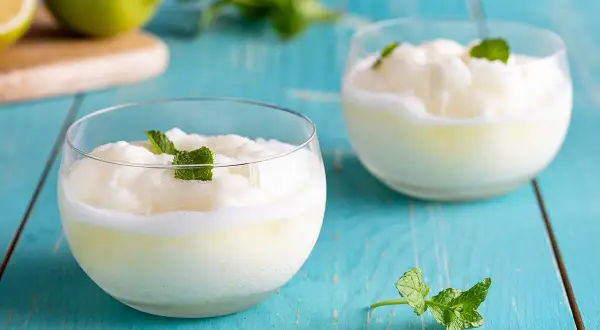 Due bicchieri di sorbetto al limone veloce, guarniti con menta fresca, su un tavolo di legno blu.