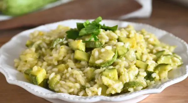 Un cremoso risotto con zucchine, guarnito con prezzemolo fresco, servito in un piatto bianco.