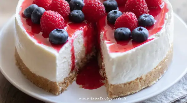 Cheesecake con mascarpone, guarnita con lamponi e mirtilli freschi, con una colata di salsa rossa.