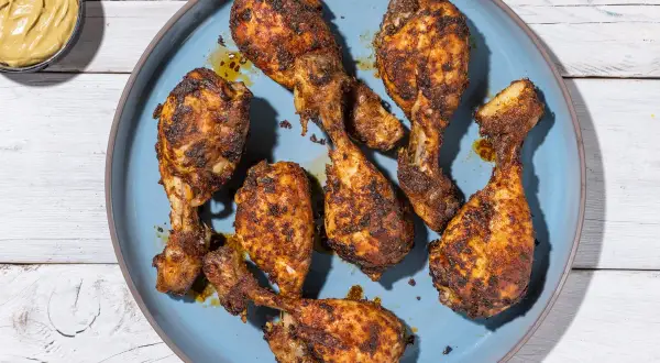 Cosce di pollo in friggitrice ad aria, dorate e succulente, servite su un piatto blu. Accanto, una ciotolina di senape.
