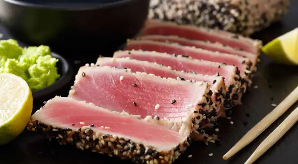Tonno scottato in crosta di sesamo, perfetto per scoprire come cucinare il tonno fresco. Servito con lime, wasabi e salsa di soia.