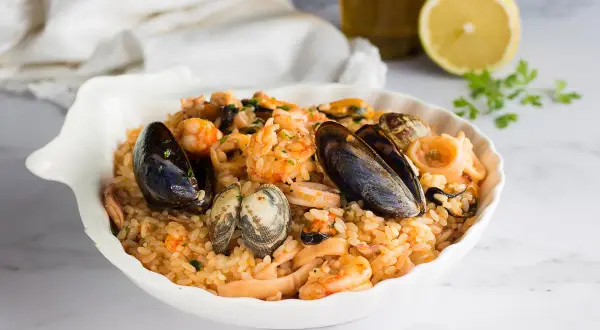 Un invitante risotto allo scoglio, ricco di cozze, vongole, gamberi e calamari, servito in una conchiglia bianca.
