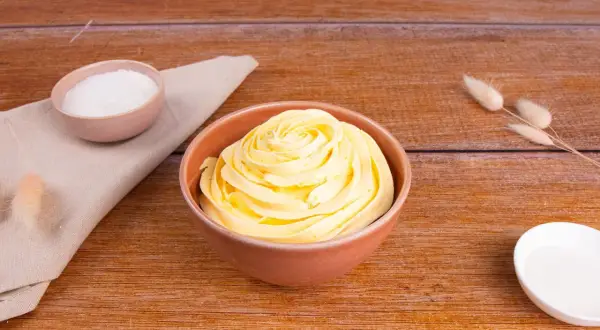Una ciotola di soffice crema al burro, pronta per decorare torte. Accanto, ciotoline con zucchero e decorazioni naturali.