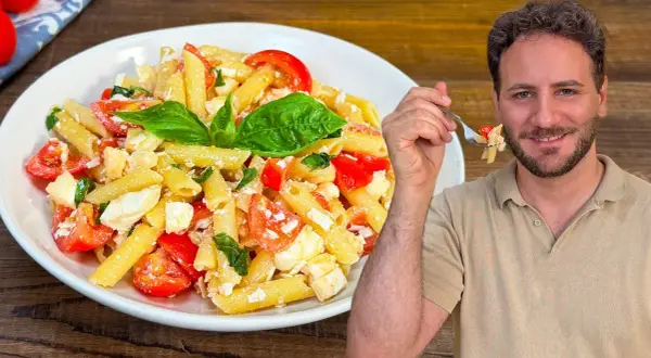 Un uomo sorride mentre assaggia una forchettata di pasta alla crudaiola, un piatto fresco con pomodorini, mozzarella e basilico.