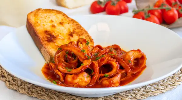 Un piatto di moscardini in umido, succulenti e profumati, accompagnati da una fetta di pane tostato e pomodorini freschi.