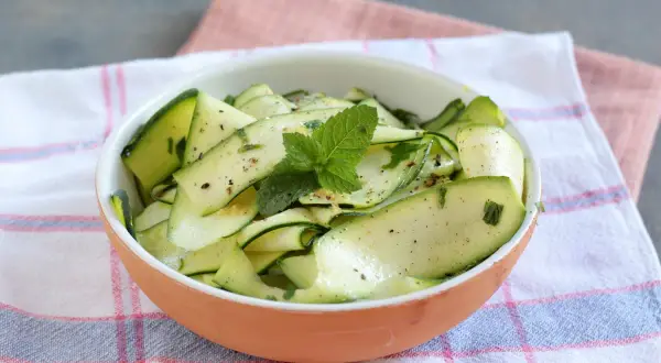 Insalata di zucchine marinate, condite con erbe aromatiche e menta fresca, servite in una ciotola di terracotta.