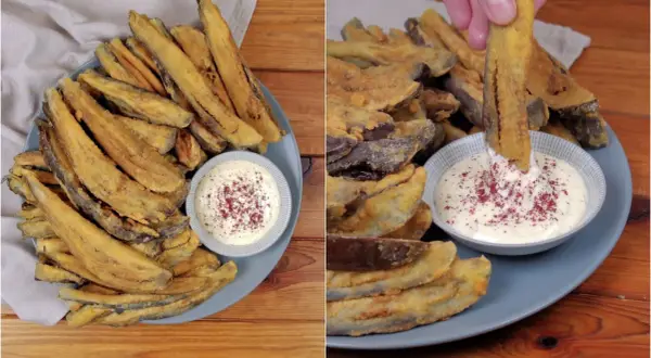 Piatto di melanzane fritte dorate e croccanti, servite con una ciotolina di salsa bianca cosparsa di spezie rosse. Una mano intinge una bastoncino di melanzana nella salsa.