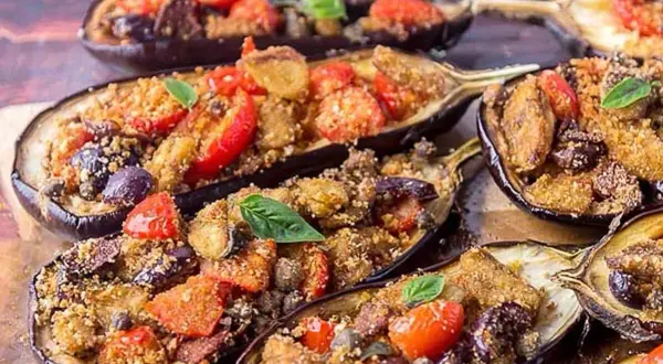 Melanzane a scarpone ripiene di pomodorini, olive e pangrattato, guarnite con basilico fresco. Un piatto saporito e invitante.