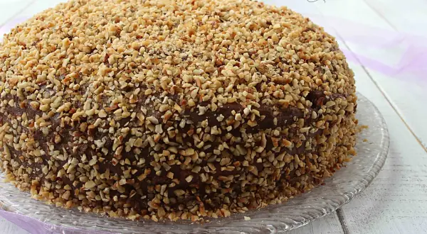 Torta ricoperta di cioccolato e nocciole tritate, una deliziosa pizza dolce abruzzese su un piatto di vetro.