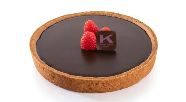 Una deliziosa crostata al cioccolato, con tre lamponi freschi e il logo di Ernst Knam.