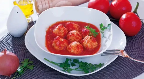 Polpette di merluzzo in salsa di pomodoro, guarnite con prezzemolo. Sullo sfondo, pomodori, cipolla e sale.