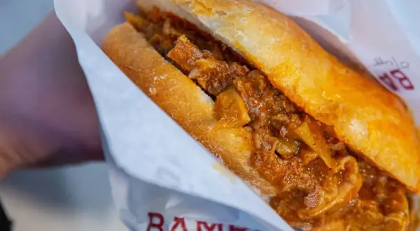 Panino con trippa alla fiorentina, un classico street food toscano, avvolto in carta con logo.
