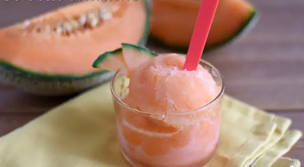 Sorbetto al melone rinfrescante in un bicchiere, con fette di melone fresco sullo sfondo.