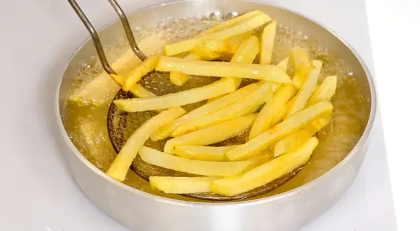 Patatine fritte dorate che sfrigolano nell'olio bollente, pronte per essere gustate.
