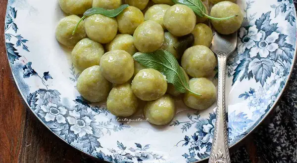 Un piatto di gnocchi di zucchine, conditi con burro e salvia, su un elegante piatto decorato.