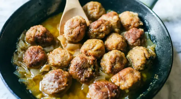Polpette in bianco cremose in padella, dorate e succulente, adagiate su un letto di cipolle caramellate.