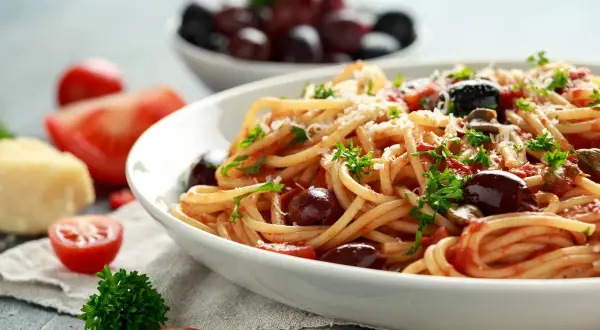 Un piatto invitante di pasta alla puttanesca, con spaghetti conditi con pomodoro, olive nere e prezzemolo fresco.