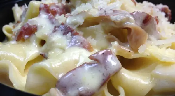 Primo piatto cremoso di pasta panna e speck, cosparso di formaggio grattugiato.