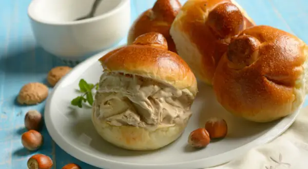 Brioche col tuppo ripieno di gelato, con nocciole e biscotti intorno.