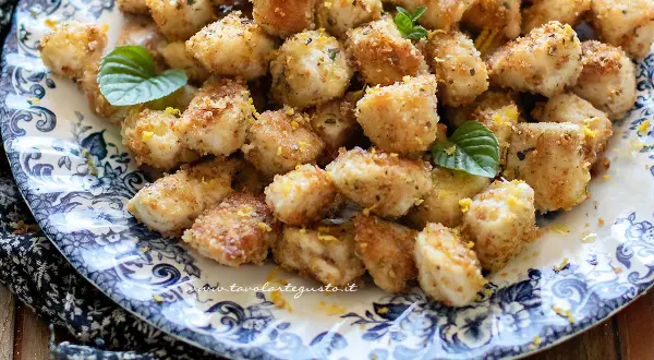 Bocconcini di pollo dorati e croccanti, guarniti con scorza di limone e foglioline di menta, serviti su un piatto decorato.