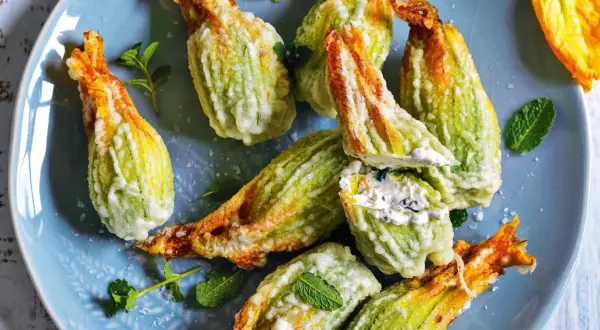 Fiori di zucca fritti, ripieni di formaggio cremoso e guarniti con menta fresca, su un piatto blu.