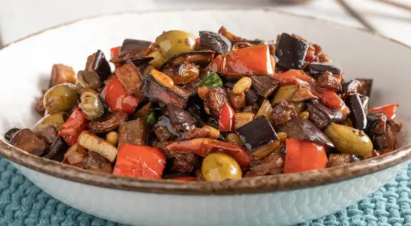 Un invitante piatto di caponata di verdure, con melanzane, peperoni rossi, olive verdi e capperi, pronto per essere gustato.