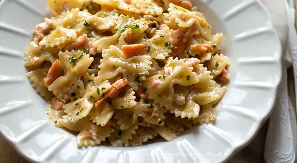 Farfalle cremose con salmone affumicato, un piatto delizioso e invitante, guarnito con prezzemolo fresco e pepe nero.