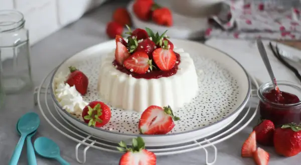 Deliziosa panna cotta con fragole fresche e salsa di fragole, guarnita con panna montata e foglioline di menta.