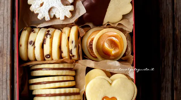 Scatola piena di biscotti al burro: a fiocco di neve, con gocce di cioccolato, ripieni di caramello e a forma di cuore.