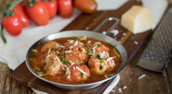 Polpette al sugo ricetta della nonna, succulente e profumate, servite in un piatto di metallo con pomodori freschi e parmigiano.