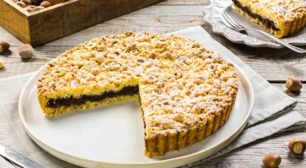 Sbriciolata alla Nutella con tante nocciole croccanti, una fetta tagliata mostra il ripieno goloso.