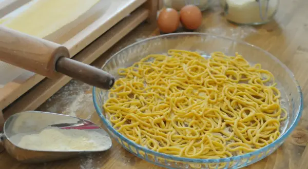 Spaghetti alla chitarra appena fatti, pronti per essere cucinati. Ingredienti freschi e attrezzi per la pasta sul tavolo.