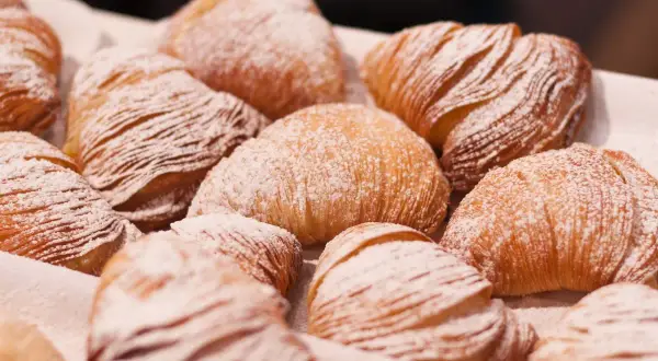Un gruppo di sfogliatella riccia, dolci napoletani con pasta sfoglia croccante e ripieno cremoso, cosparsi di zucchero a velo.