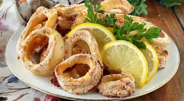 Anelli di calamari gratinati al forno, dorati e croccanti, guarniti con spicchi di limone e prezzemolo fresco.