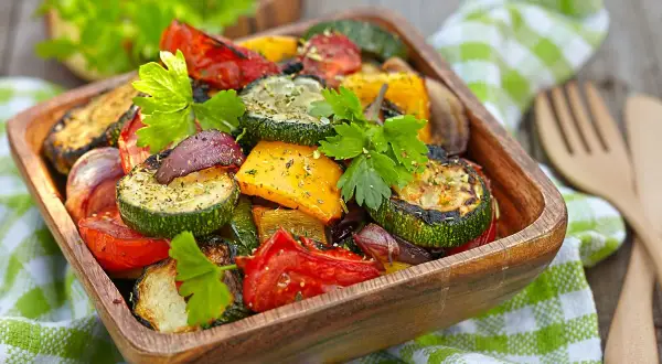Un misto colorato di verdure in friggitrice ad aria, tra cui zucchine, peperoni e pomodori, guarnito con prezzemolo fresco.