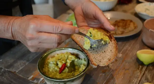 Mani che spalmano la salsa guacamole ricetta su una fetta di pane tostato. Un peperoncino rosso decora la ciotola.