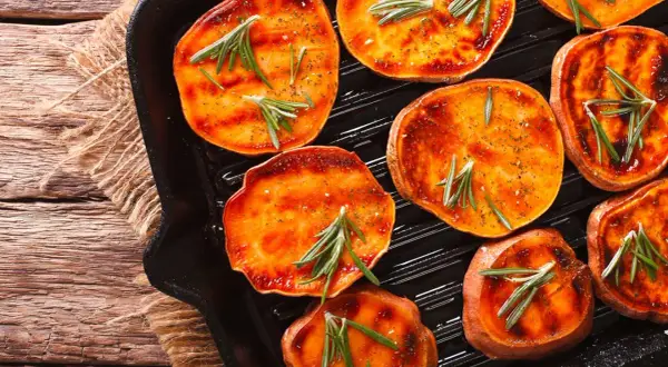 Fette di patate dolci grigliate in padella con rosmarino e spezie, pronte per essere gustate.