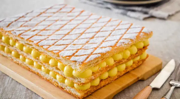 Una deliziosa torta millefoglie con strati di pasta sfoglia e crema pasticcera, cosparsa di zucchero a velo.